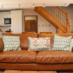 soffa lledr i dri person gyda cegin a grisiau tu nol