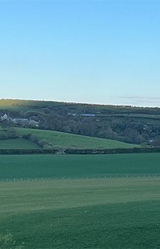 Golwg bell o'r caeau ar tai gyda awyr las yn y cefndir